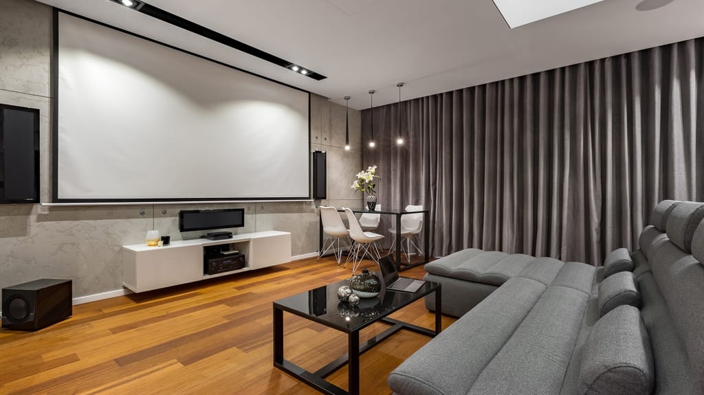 Modern home theater with projector screen and gray sectional sofa in a basement