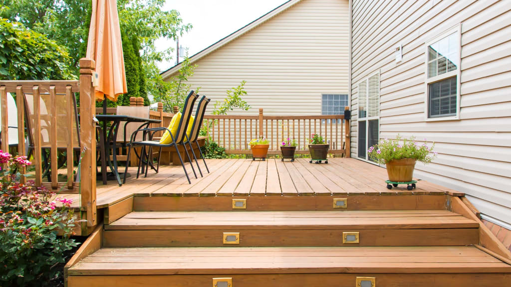 Patio en bois teint foncé, table et trois chaises blanches attenant à une maison de style moderne, très fenestrée