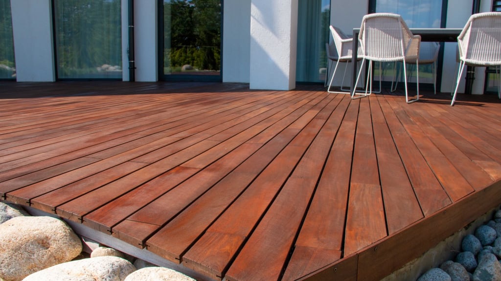 Terrasse en bois exotique teinte rouge brune avec table et chaises blanches