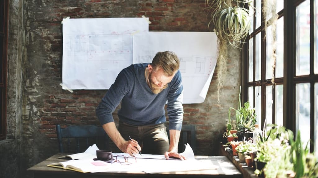 architecte debout devant table de travail dessinant plans
