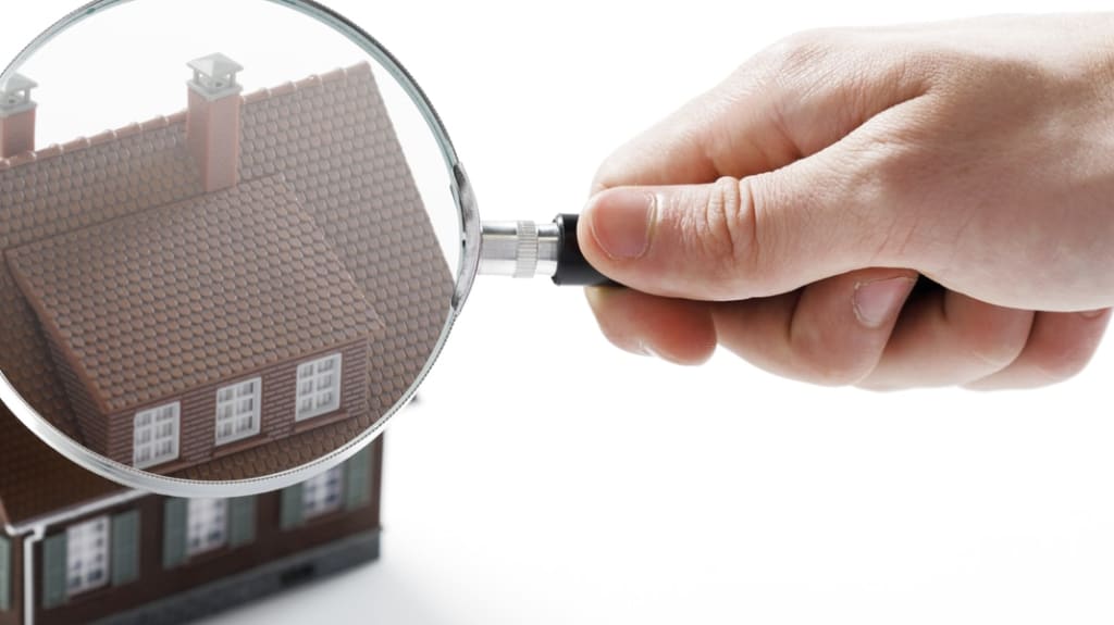 main d'homme examinant à la loupe une maison pour détecter des problèmes d'enveloppe du bâtiment