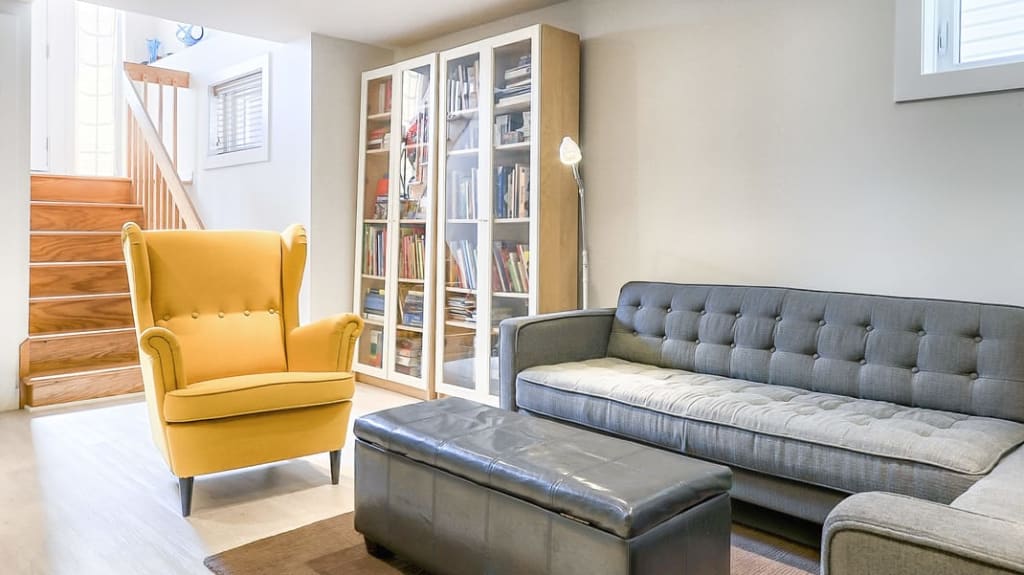 Photo après - rénovation de sous-sol - Projet Allard avec fauteuil jaune, divant gris et plancher pâle