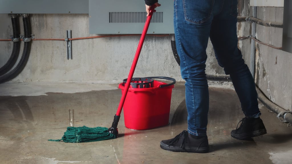 Personne qui nettoie un dégât d'eau causé par une inondation au sous-sol avec une vadrouille et un seau