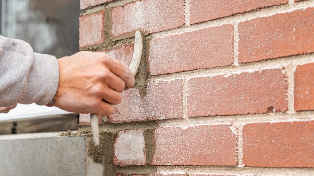 Hand of a bricklayer repairing joints of a red brick wall