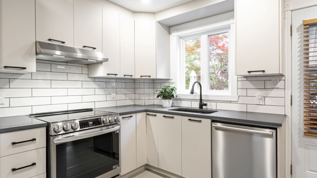 Cuisine classique blanche avec vue sur armoires blanches, dosseret de céramique blanche, cuisinière et lave-vaisselle en acier inoxydable et plancher de céramique blanche.