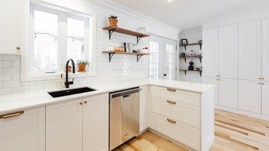 White kitchen with brass hardware, open wood shelving, and plants in a contemporary home