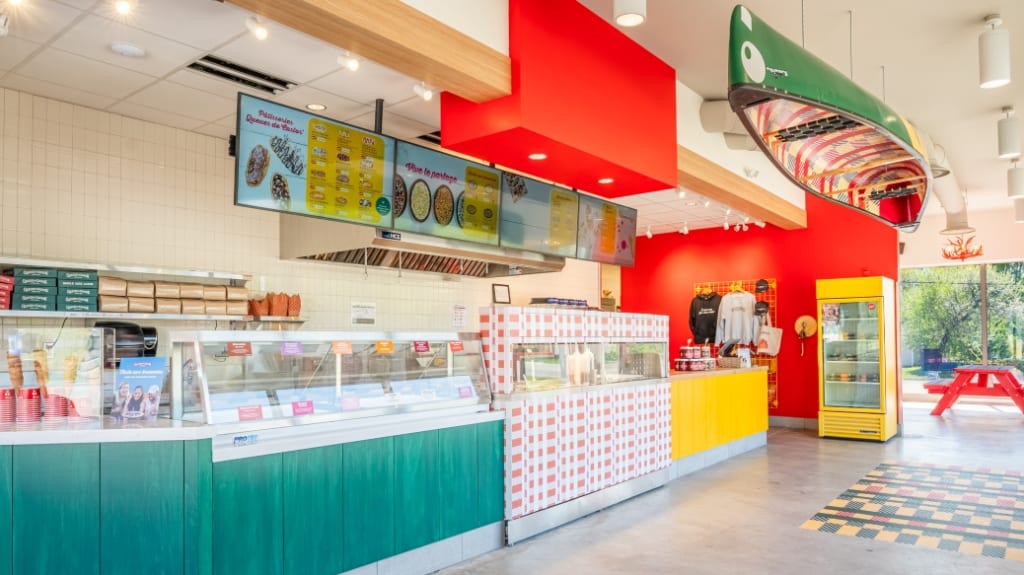 Newly renovated BeaverTails location featuring a split-complementary colour palette, digital menu boards, concrete floor, and a canoe suspended from the ceiling.