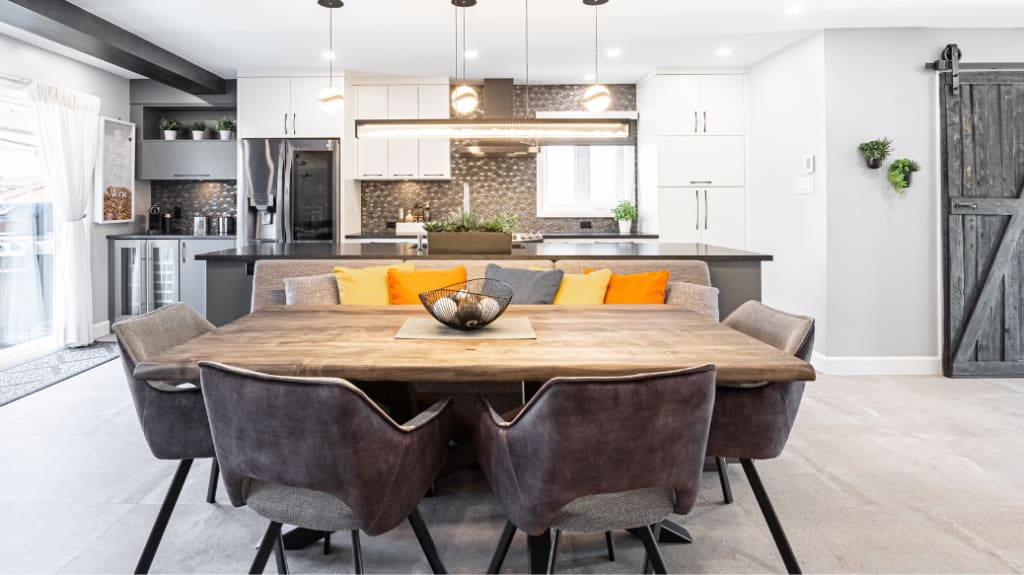 Cuisine à aire ouverte avec table de chêne, banquette, ilot central, chaises-fauteuils et coussins colorés