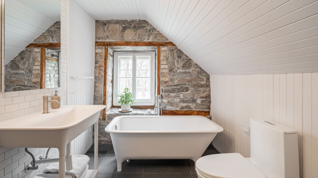 Salle de bain rustique rénovée dans maison patrimoniale avec bain autoportant, vanité sur pattes et mur de pierre d