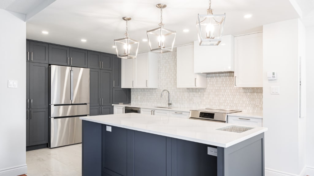 Renovated kitchen with centre island, white veined quartz countertop, dark grey cabinets, and pendant lighting in multiple renovation project