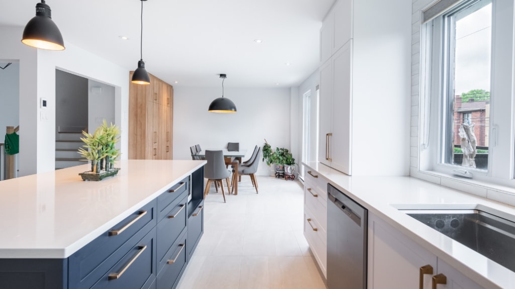 cuisine moderne à air ouverte rénovée avec grand ilot en quartz, plancher en céramique effet sable et cuisinette