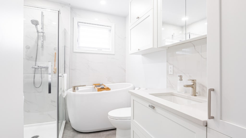 Small renovated bathroom with white walls, a freestanding bathtub, and a walk-in shower with marble tiles