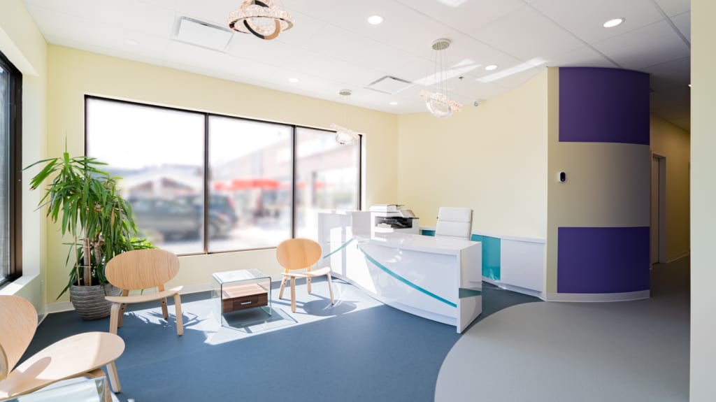 Clinic reception with big windows, pastel yellow walls, and blue and purple accents