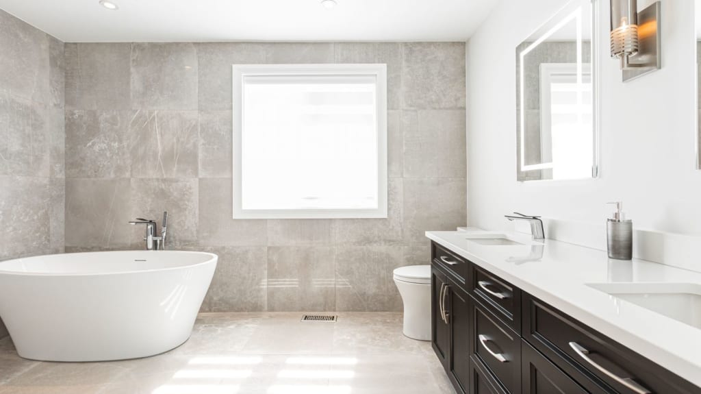 A neutral-coloured bathroom with a freestanding tub, toilet, and a dark double vanity