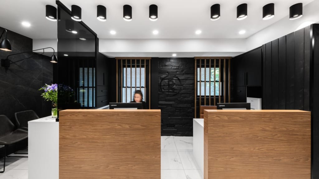 Une réception dentaire style contemporain, avec sols en marbre blanc, murs noirs, et un bureau de réception en bois.