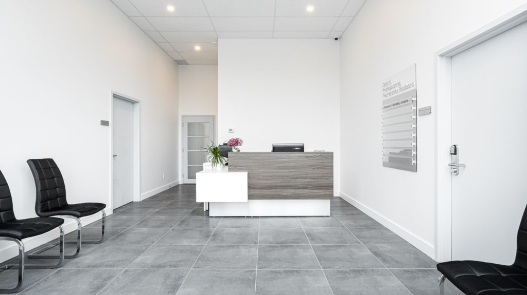 office reception area with black leather chairs, white walls, grey tile floors, and a two-tone reception desk