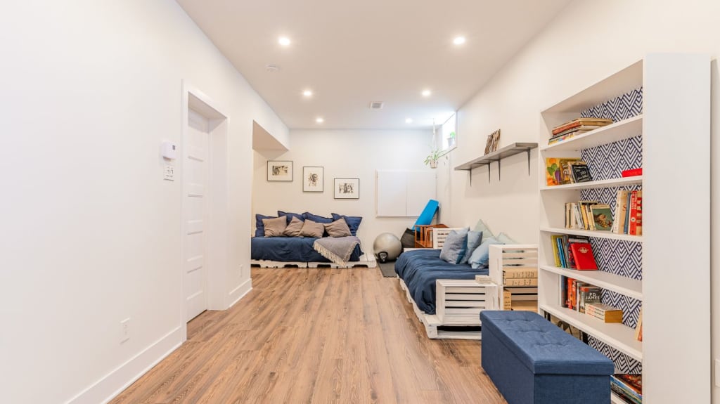 A beautiful renovated basement featuring wooden floors, blue couches, and a lovely bookshelf