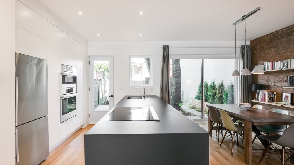 cuisine rénovée moderne blanche avec grand îlot et mur de brique dans la salle à manger