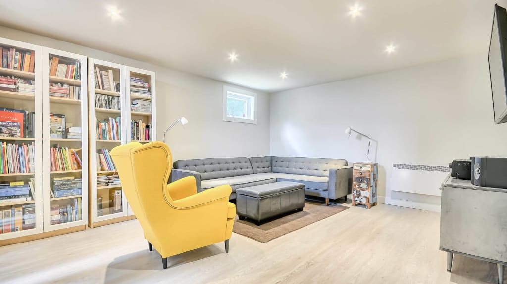 décoration de sous-sol avec bibliothèque, chaise jaune et divan en L gris