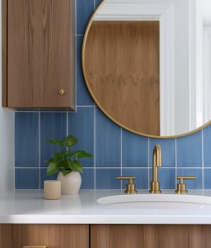 Tuiles verticales bleues servant de dosseret de salle de bain, armoires en bois et robinetterie dorée