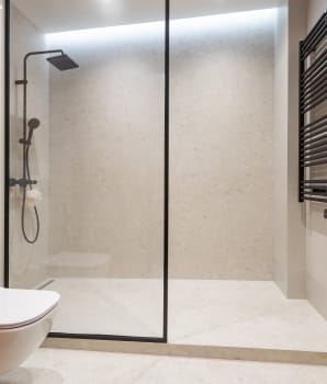 Carrelage gris et blanc dans la douche et sur le sol d’une salle de bain avec cloison en verre, toilette et porte-serviette