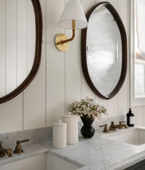 Lambris beige pâle servant de dosseret sur le mur d’une salle de bain décorée de miroirs noirs et de pots en céramique