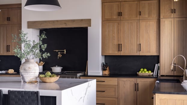 Wooden cabinets with backsplash and black handles in a kitchen with gold hardware