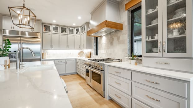 White countertops, stainless steel appliances and grey cabinets with silver handles