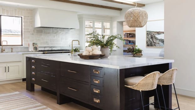 Hanging light fixture and rattan chairs, large dark island and plaster hood on stone wall 