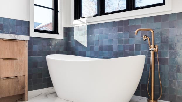 Baignoire autonome et robinetterie dorée devant un mur de tuiles bleues