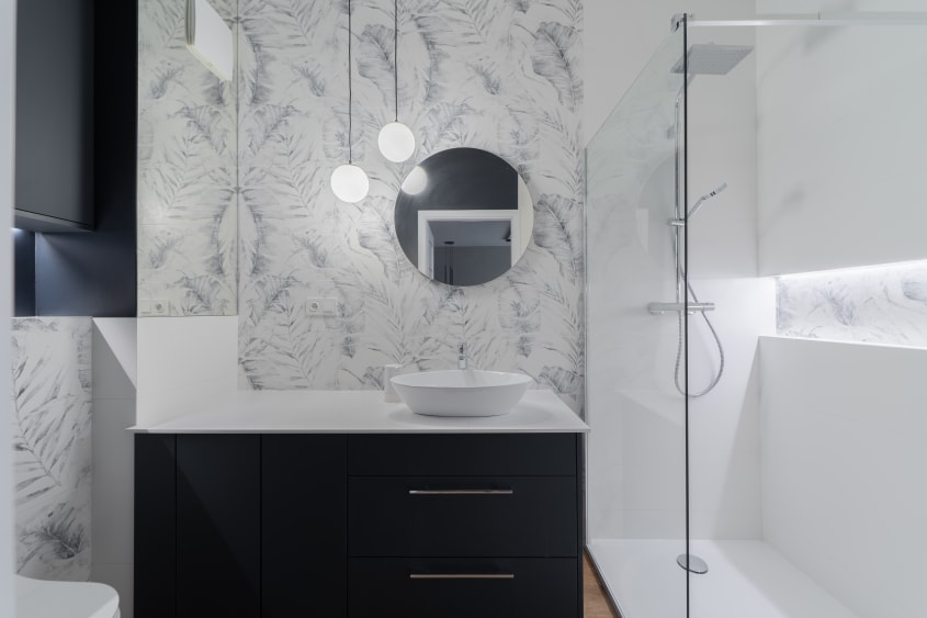Douche vitrée dans le coin d’une salle de bain avec tapisserie et luminaire suspendu au-dessus de la vanité