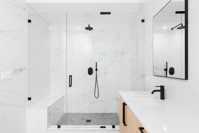 Robinetterie de salle de bain noire incluant un pommeau de douche fixe dans une grande douche en verre