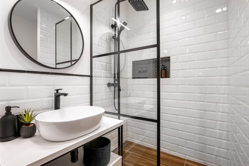 Cloison vitrée aux contours noirs dans une douche aux murs de briques blanches 