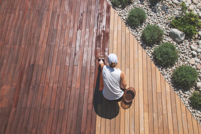Top-down view of a woman staining a wooden deck with a brush