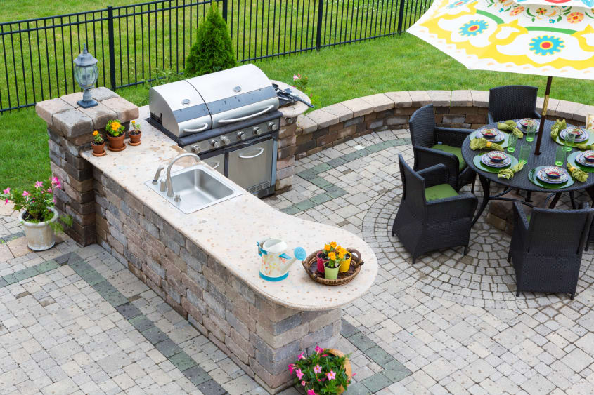 Stone deck featuring a gas barbecue, built-in sink in an island, black patio furniture with flower-printed sunshade