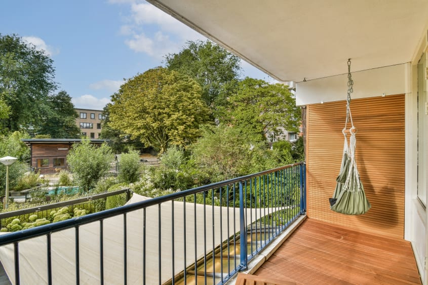Un balcon paisible et longiligne au revêtement de bois baigné de lumière et offrant une vue sur le voisinage et les arbres et arbustes avoisinants