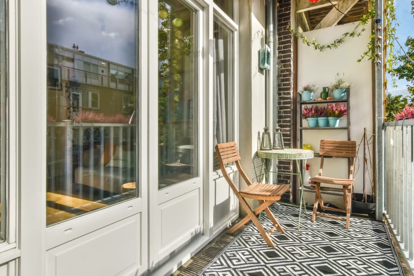 Petit balcon fait en longueur avec chaises de teck, petite table circulaire et étagère garnie de plantes