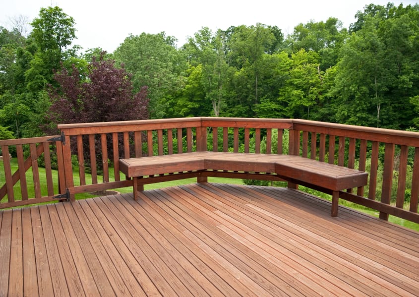 Spacious wooden deck with built-in seating along the railing, backyard full of trees