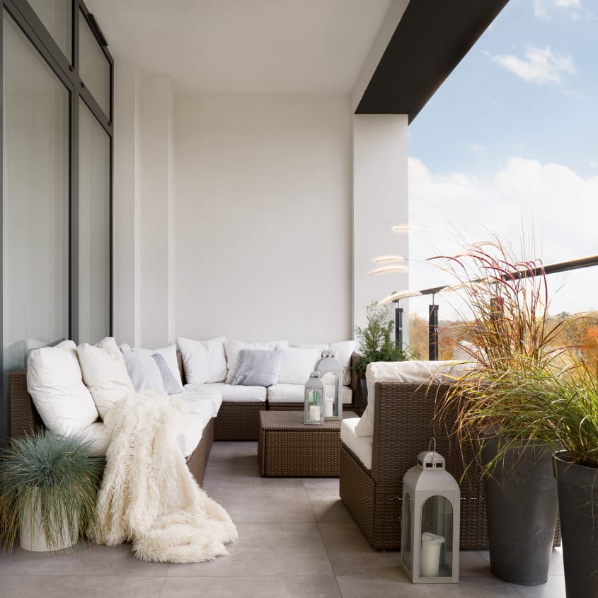 Small balcony with cozy rattan furniture, plants, lantern and blanket