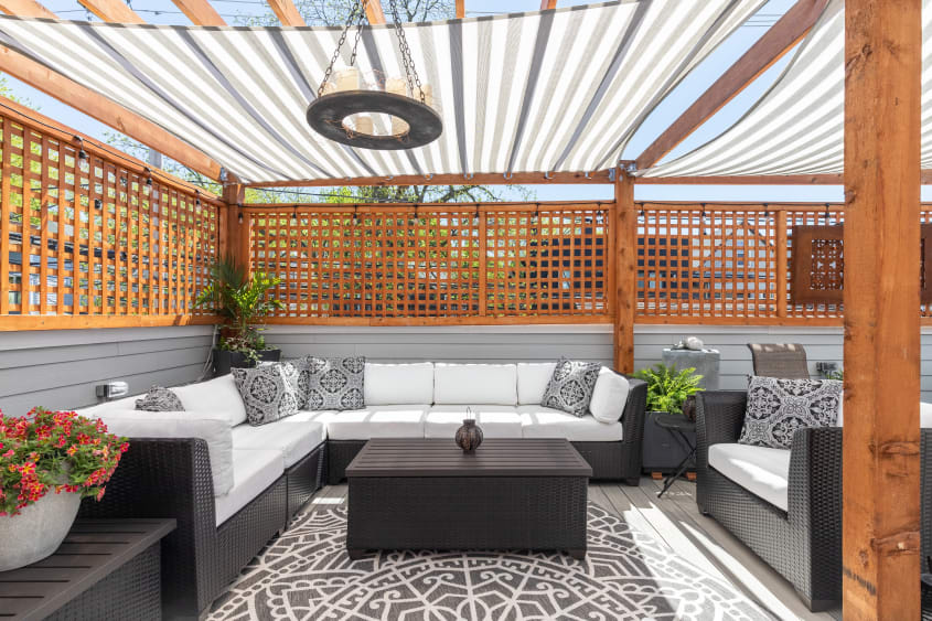 Cozy deck area with large couches, pergola with striped shade fabric, wooden lattices