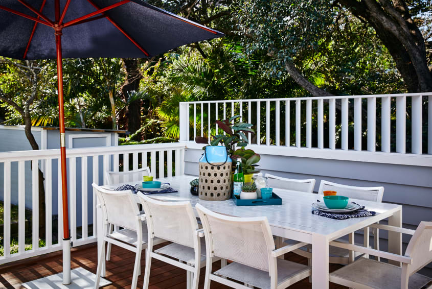 Coastal style backyard deck with a white dining table setup, navy blue sunshade