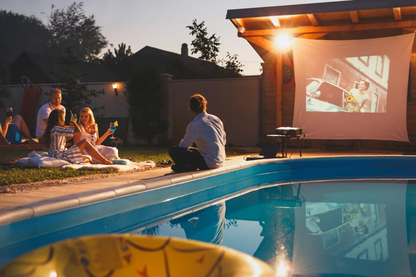Group of people watching a projector screen in the backyard by the pool