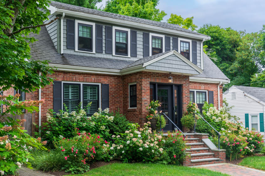 Red brick house with gray roof surrounded by outdoor plants