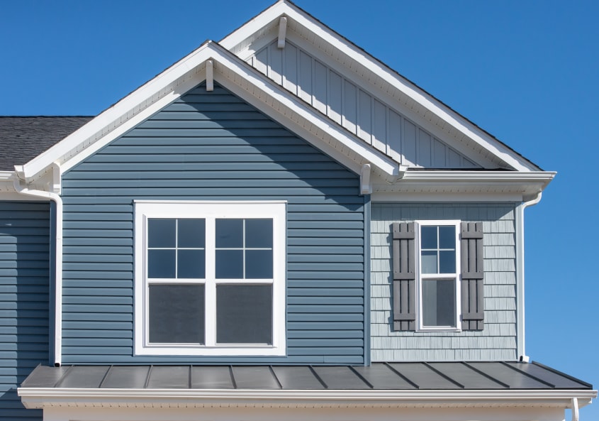 Close up view of exterior blue vinyl siding on the top floor of a house