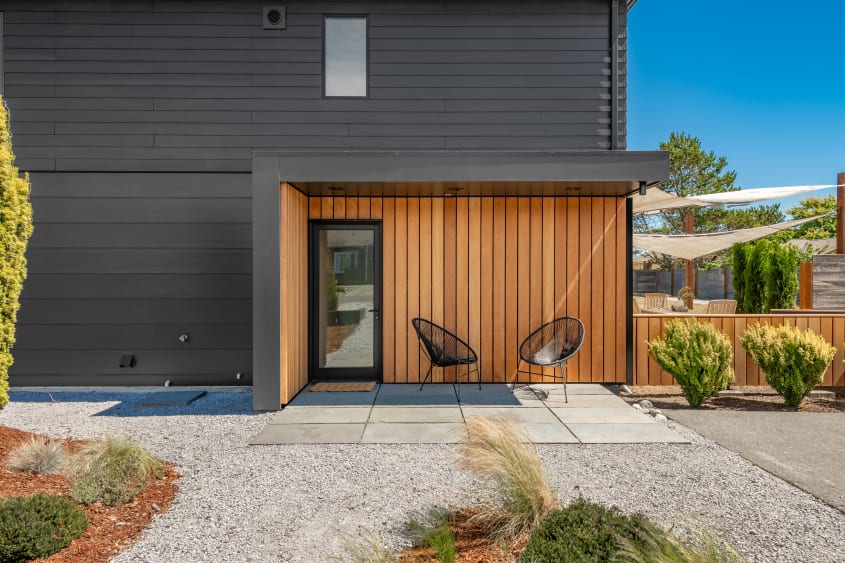 Contemporary house exterior with black recycled metal shingles and cedar shingles, featuring two black patio chairs