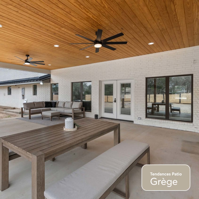 Grand patio en ciment de couleur grège avec meubles de salle à manger extérieur, toiture en bois et ventilateurs