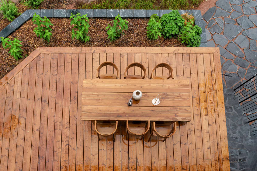 Terrasse, table et chaises en bois vue de haut, adjacent à des plantes et à un terrassement en pierre