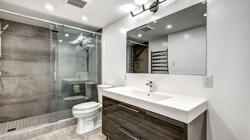 Salle de bain contemporaine avec douche vitrée, mur de carrelage gris, toilette et meuble-lavabo en bois foncé