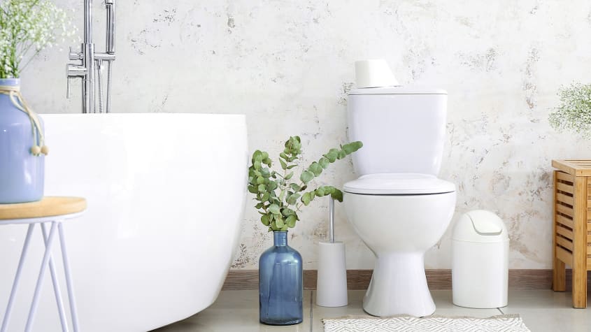 Baignoire autoportante et toilette blanche devant le mur texturé d’une salle de bain incluant des accessoires décoratifs