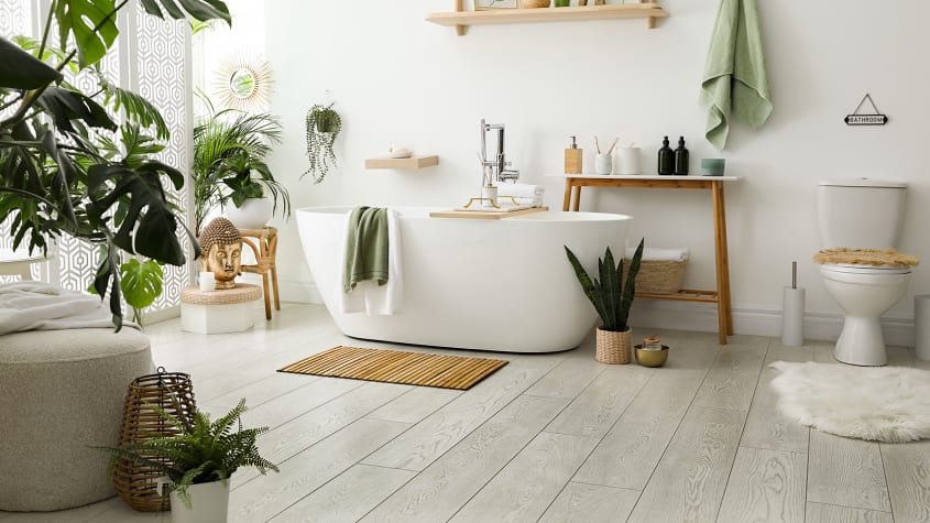 Baignoire blanche, plantes et accessoires en bois sur un plancher de salle de bain gris pâle